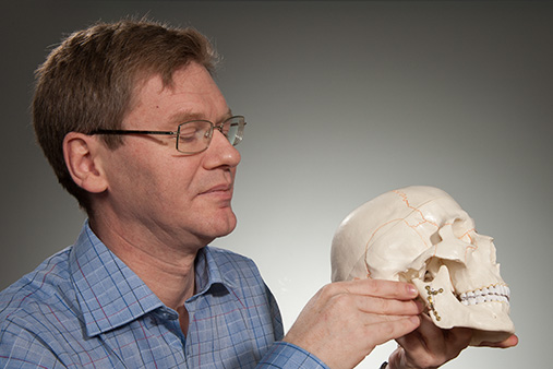 Nærbilde av Hågensli som holder en hodeskalle som har den aktuelle operasjonenn i kjeveleddet. Hågensli peker mot operasjonspunktet.