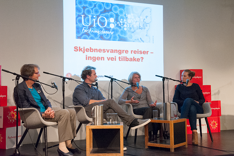 Bilde av fire forskere som sitter i lenestoler på et podium, med mikrofoner foran seg og bak dem på veggen er tittelen på arrangementet projisert: Skjebnesvangre reiser - ingen vei tilbake?