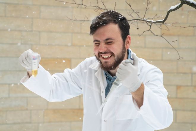 Mann i hvit frakk ler utendørs mens det snør