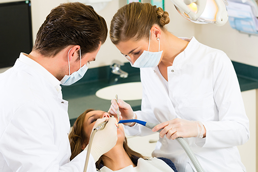 Illustrasjonsfoto av to tannleger som behandler en pasient som ligger i tannlegestolen.