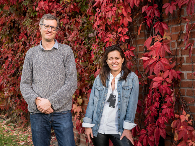 The two scientists looking happy outside, in front of a bright, autumn red hedge