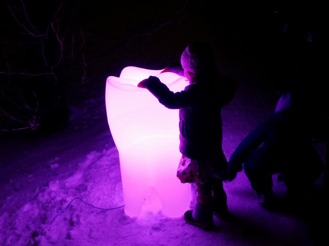 Et barn står og holder oppå en plasttann like stor som barnet, som lyser opp i rosa