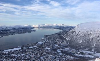 Oversiktsbilde av Tromsø by, liggende inntil en fjord, med fjell på den andre siden.