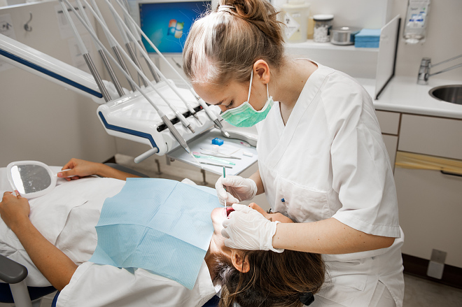 Tannlegestudent med grønt munnbind bøyd over pasient