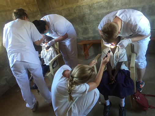 Bilde av fire tannpleiestudenter som undersøker Tanzanianske skolebarn.
