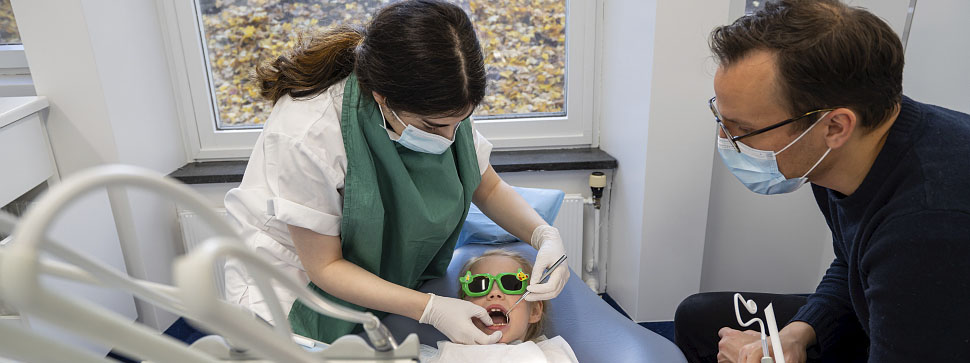 Tannlege behandler barn. Barnets pappa følger med på sidelinjen